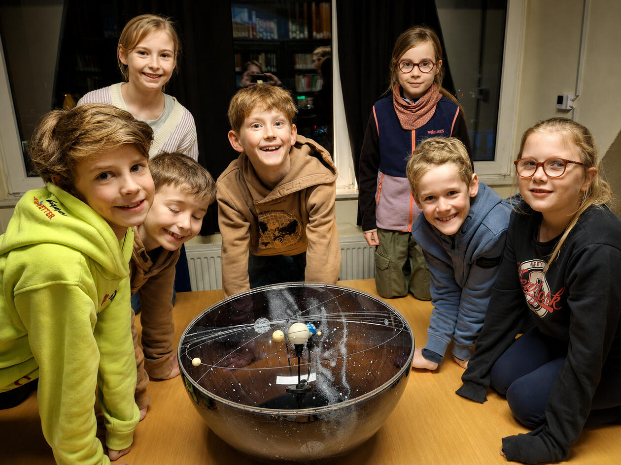 Mehrere Kinder stehen begeistert um ein Planetarium und beobachten die Bewegung der Planeten während einer spannenden Astronomie-Vorführung.